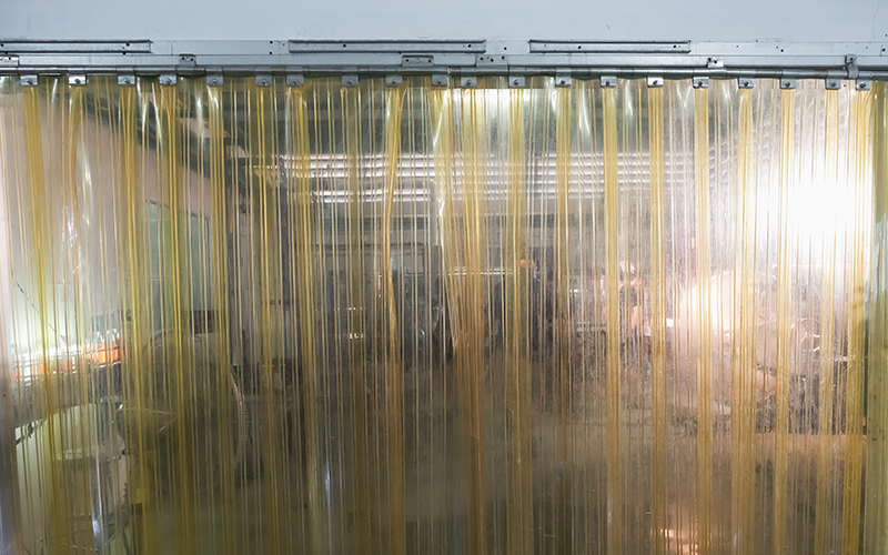 Plastic strips hanging from a rail in a warehouse to prevent contaminants and air from passing through Air Curtain Barrier